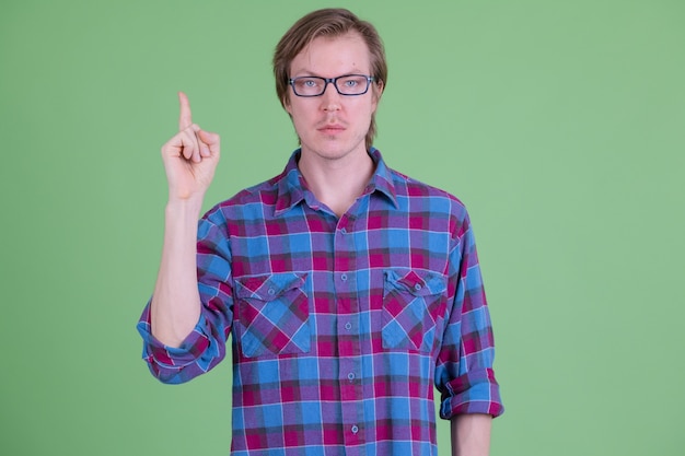 Portrait of young handsome Scandinavian hipster man with eyeglasses against chroma key or green wall