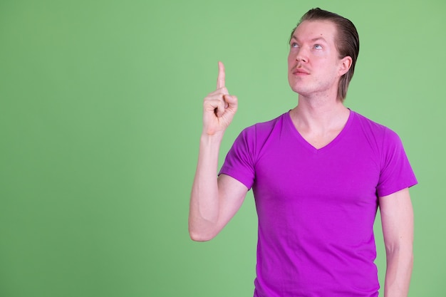 Portrait of young handsome Scandinavian man wearing purple shirt against chroma key or green wall