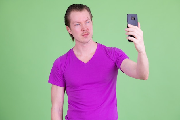 Портрет молодого красивого скандинавского мужчины в фиолетовой рубашке на фоне цветного ключа или зеленой стены