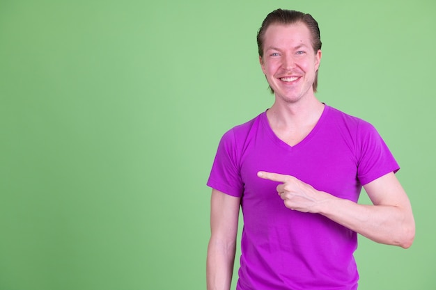 Portrait of young handsome Scandinavian man wearing purple shirt against chroma key or green wall