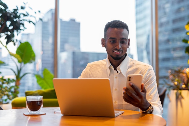 Portrait of young handsome stylish black man using laptop computer in coffee shop