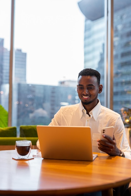 Portrait of young handsome stylish black man using laptop\
computer in coffee shop