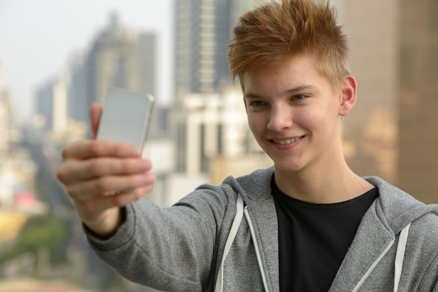 Portrait of young handsome teenage boy against view of the city outdoors