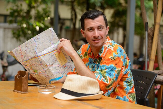 Portrait of young handsome tourist man at restaurant in the city outdoors