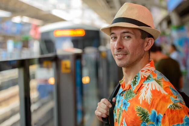 Portrait of young handsome tourist man at sky train station in the city