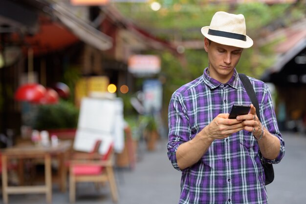 Portrait of young handsome tourist man using phone in the streets