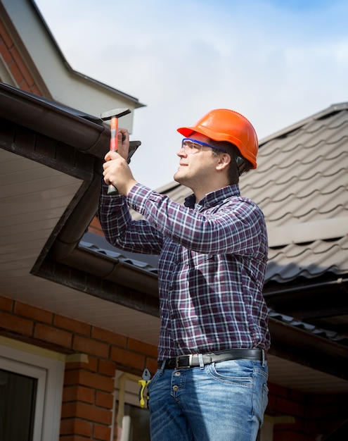 Portrait of young handyman repairing house roof with nails and hammer