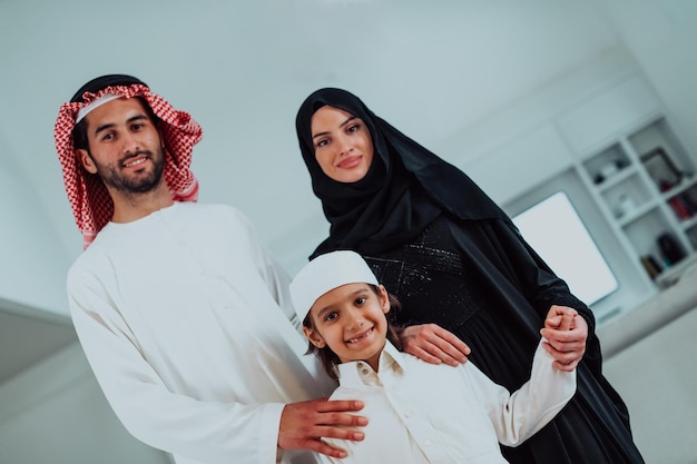 портрет молодой счастливой арабской мусульманской семейной пары с сыном в традиционной одежде, проводящей время вместе в месяц рамадан дома. Фото высокого качества