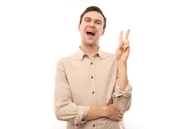 Portrait of young happy caucasian man in casual showing peace and love gesture with fingers isolated on white studio background