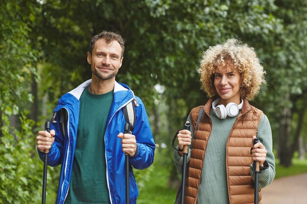 Portrait of young happy couple smiling at camera during their hiking in the forest in summer day