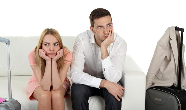 Photo portrait of young happy couple with baggage sitting on sofa isolated on white