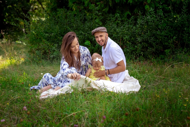 Portrait of young happy family plays with their liitle baby daughter at the green meadow