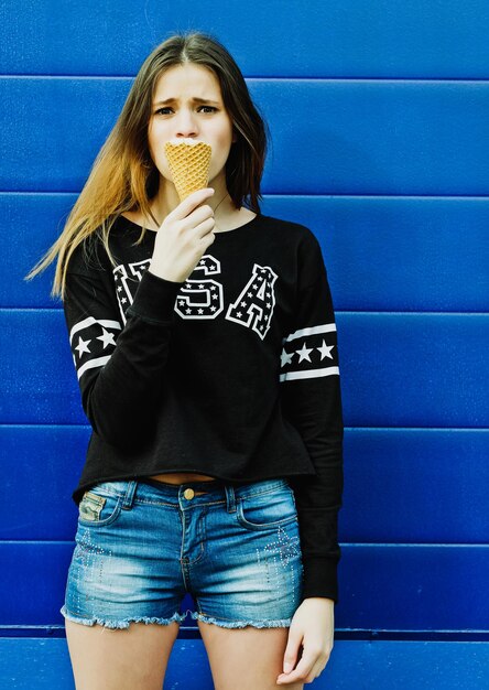 Portrait of young happy girl eating ice-cream, outdoor, over blue wall background