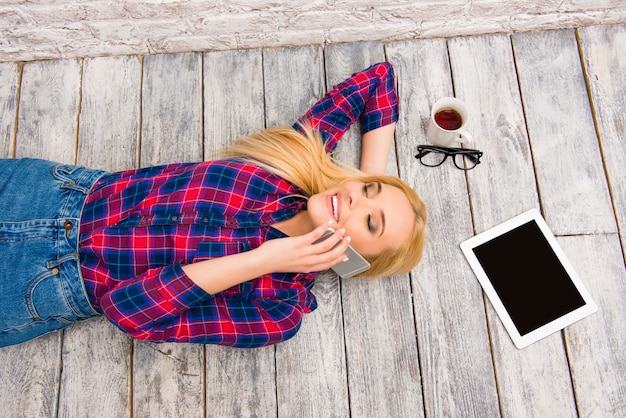 Portrait of young happy girl lying on floor and talking on phone