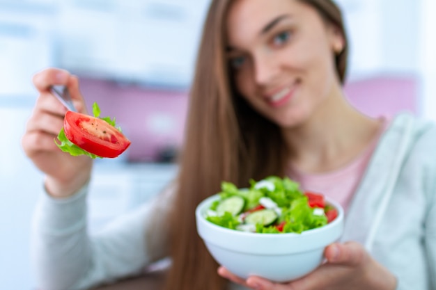 自宅で新鮮な野菜サラダを食べる若い幸せな健康な女性の肖像画。食べ物をきれいにして管理する