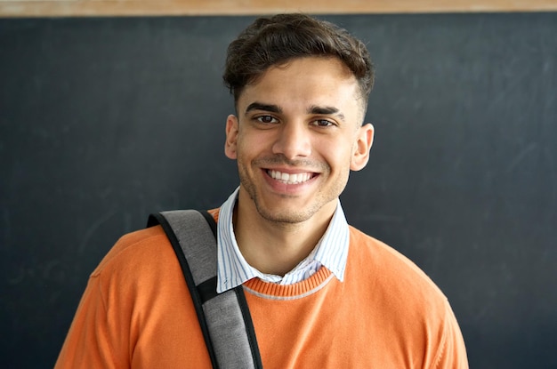 Foto ritratto di giovane studente latino felice in piedi in aula che guarda l'obbiettivo