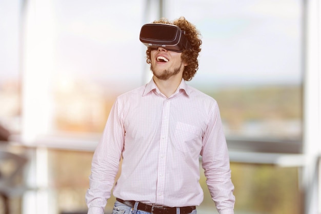 Portrait of young happy man with curly hair wearing vr headset indoor window in the background