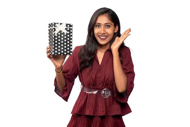 Photo portrait of young happy smiling girl in red dress holding and posing with gift box on white background
