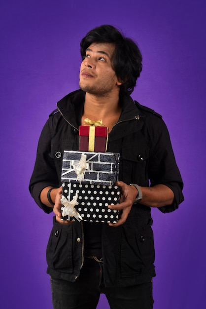 Portrait of young happy smiling handsome man holding gift box on a purple background