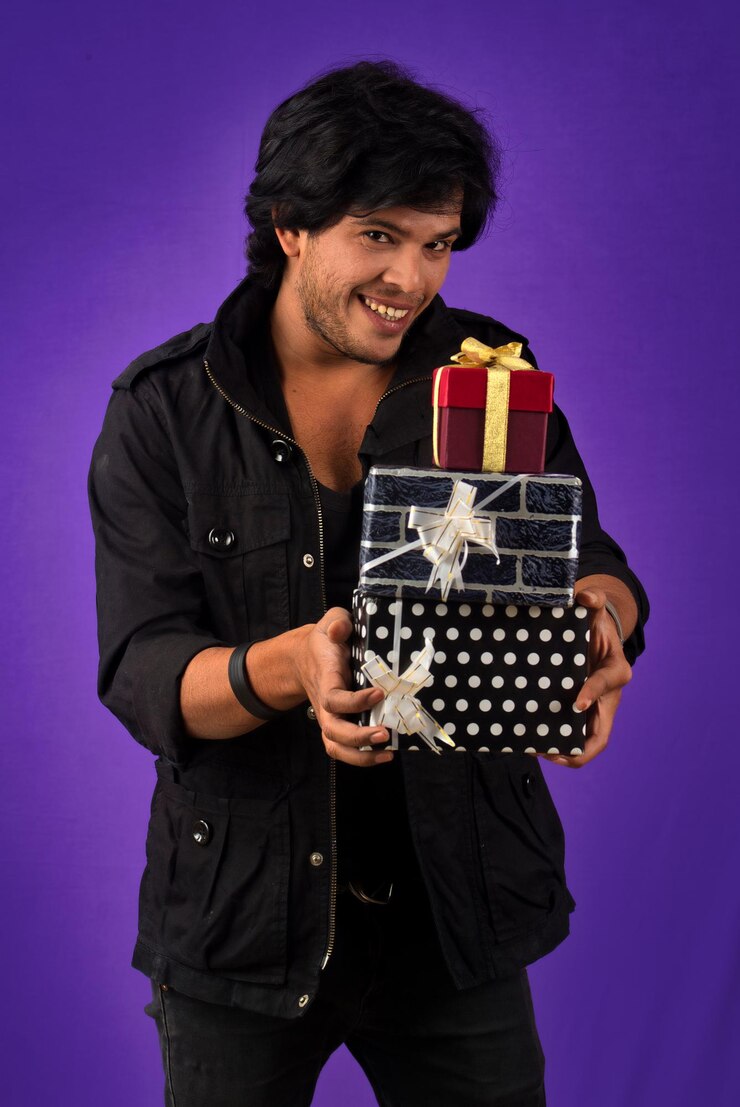 फोटो portrait of young happy smiling handsome man holding gift box on a purple background