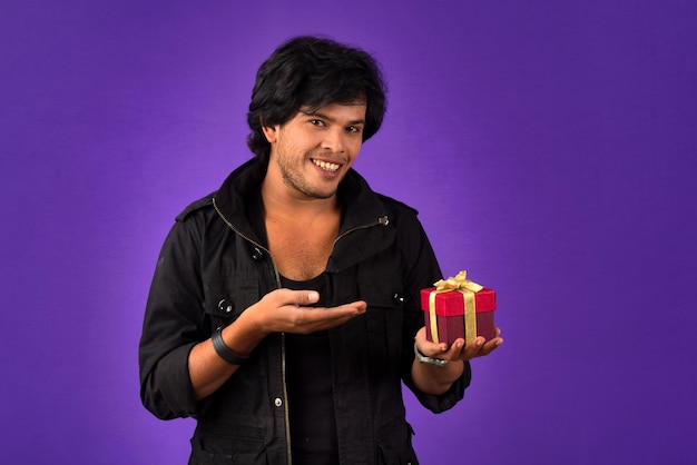 Portrait of young happy smiling handsome man holding gift box on a purple background