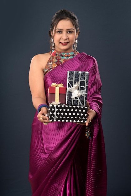 Portrait of a young happy smiling woman wearing a saree holding gift box on a grey background