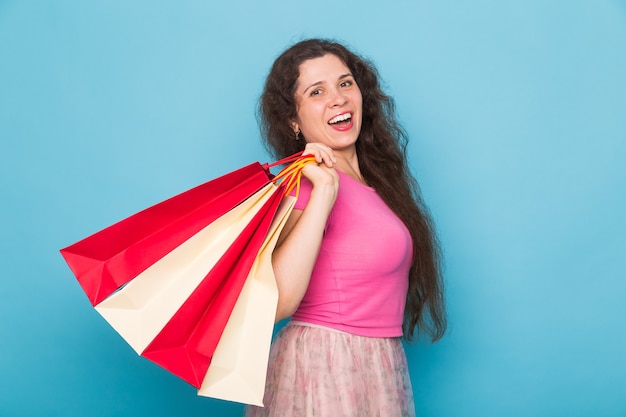 Portrait of young happy smiling woman with shopping bags, over blue background. Purchase, sale and people concept.