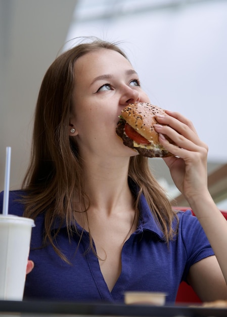 Foto ritratto di una giovane donna felice o di una bella adolescente che mangia cibo spazzatura veloce, hamburger gustosi e