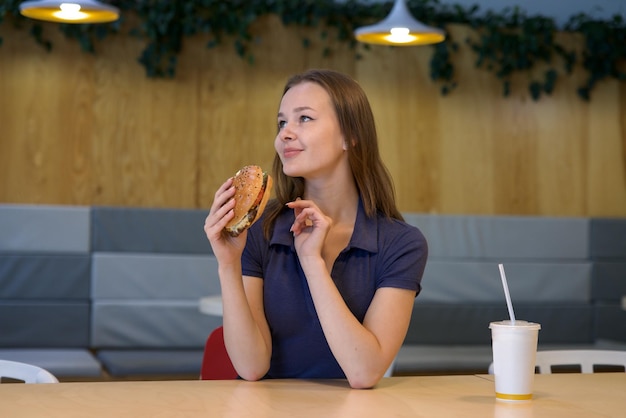 Foto ritratto di una giovane donna felice o di una bella adolescente che mangia cibo spazzatura veloce, hamburger gustosi e