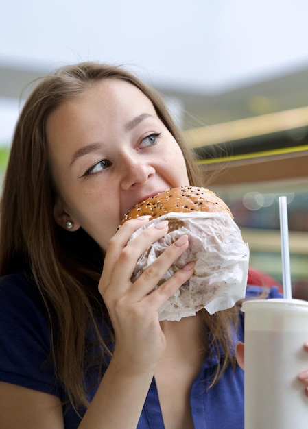 Foto ritratto di una giovane donna felice o di una bella adolescente che mangia cibo spazzatura veloce, hamburger gustosi e