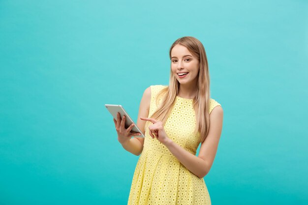 Portrait of a young happy woman holding tablet computer with copy space while standing isolated over blue background person