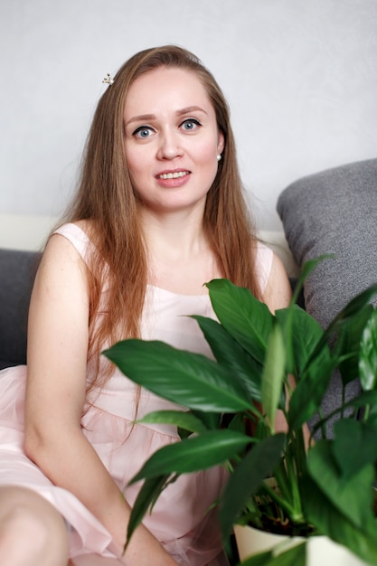 Portrait of young happy woman at home, sitting on the couch with green fresh houseplant,