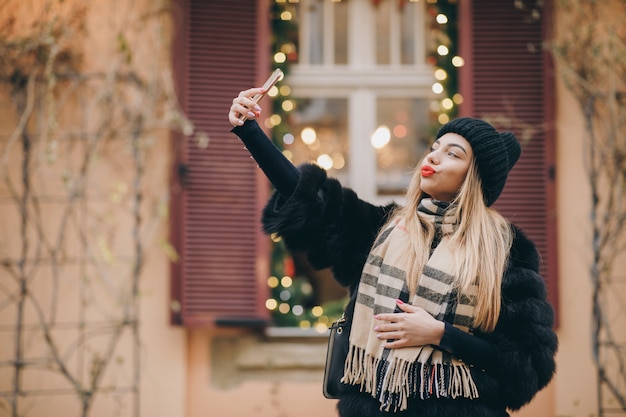 Ritratto di giovane donna felice che indossa abiti invernali in stile francese, in posa nelle strade