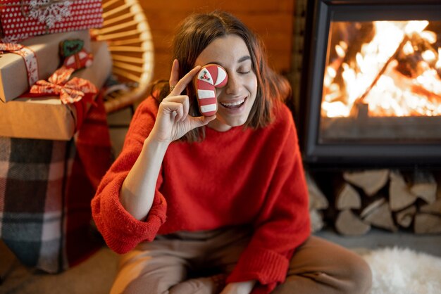 Портрет молодой счастливой женщины с рождественскими конфетами у камина во время зимних праздников