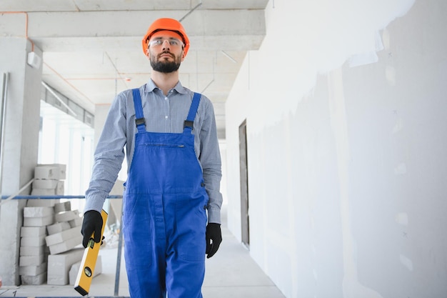 大きな未完成の部屋の建物のコンセプトでポーズをとる若くて勤勉な建設業者のポートレート