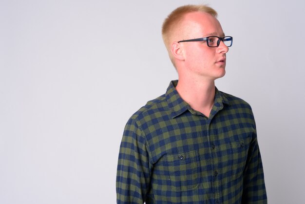 Portrait of young hipster man with blond hair wearing eyeglasses against white wall