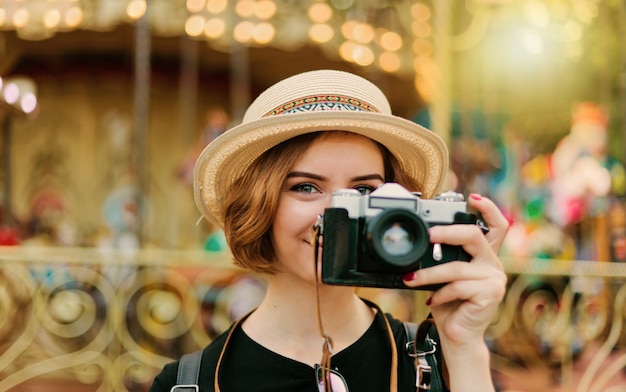 Portrait of a young hipster woman in a hat with a retro camera in an amusement park