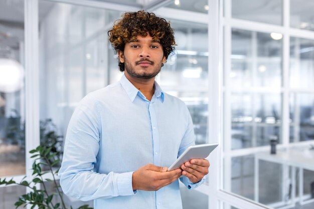 Portrait of a young hispanic male student in a blue shirt standing in the campus office with a