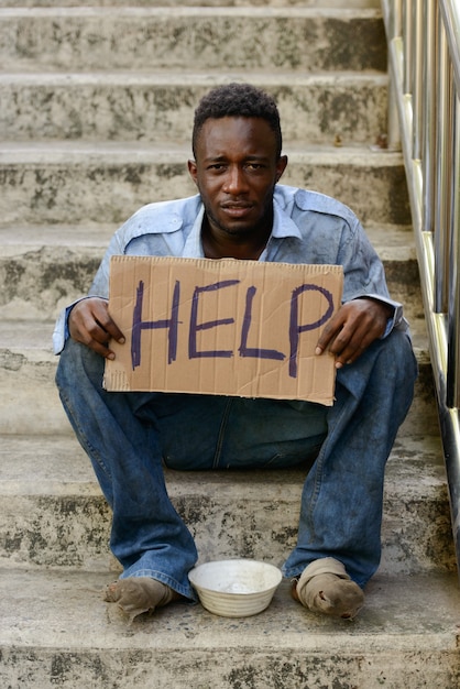 Portrait of young homeless African man on stairs in the streets outdoors