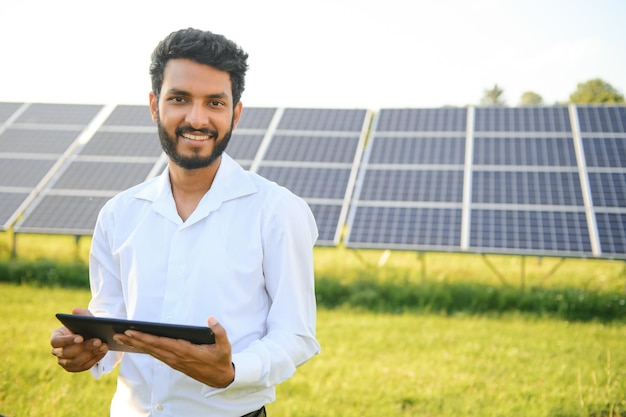 Portrait of Young indian male engineer standing near solar panels with clear blue sky background Renewable and clean energy skill india copy space