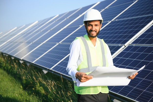 Portrait of Young indian male engineer standing near solar panels with clear blue sky background Renewable and clean energy skill india copy space