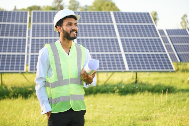Портрет молодого индийского техника или менеджера в официальной одежде, стоящего с солнечной панелью, человек с возобновляемой энергией, стоящий с перекрестными руками.