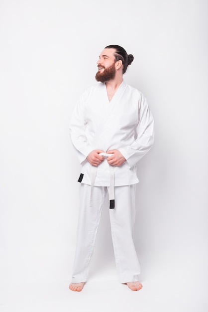 Portrait of young instructor man wearing taekwondo uniform smiling and looking aside