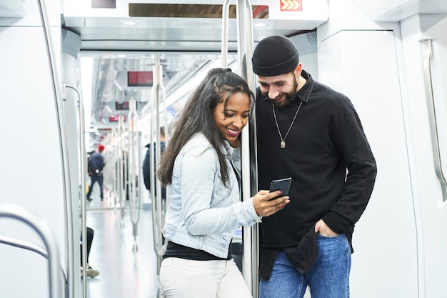 Портрет молодой межрасовой пары, использующей свой мобильный телефон в вагоне метро