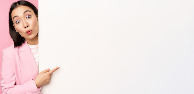 Photo portrait of young japanese business woman corporate lady in suit pointing on wall with chart showing diagram or advertisement on empty copy space pink background