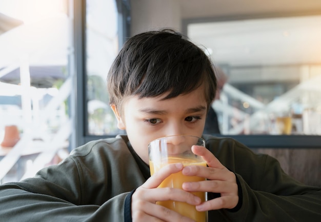 Portrait Young kid drinking fresh orange juice for breakfast in cafe Happy child boy drinking glass of fruit juice while waiting for food in restaurant Healthy food lifestyle concept