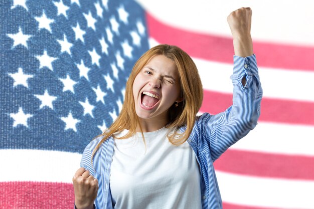 Portrait of a young lady on the background of the USA flag Concept of patriotism An emotional girl