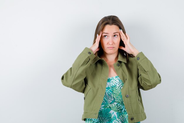 Portrait of young lady rubbing temples in green jacket and looking thoughtful front view