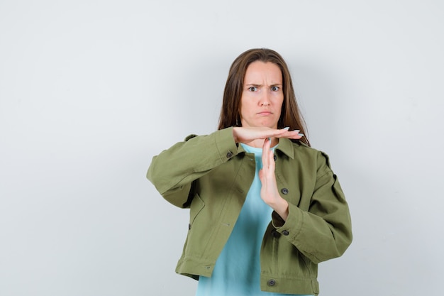 Portrait of young lady showing time break gesture in green jacket and looking sulky front view