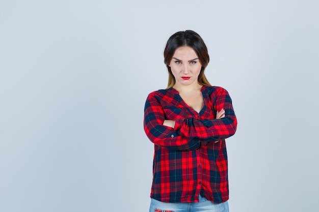 Portrait of young lady standing with crossed arms in checked shirt and looking uncertain front view